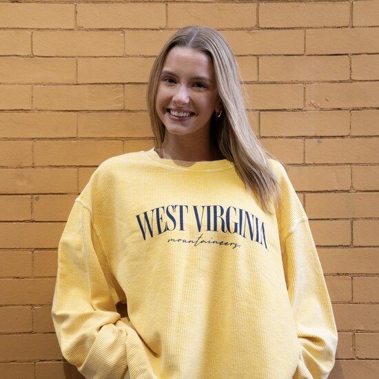 Model wearing the gold corded chickad WVU crew sweatshirt with large navy West Virginia script over navy Mountaineers in small cursive print.
