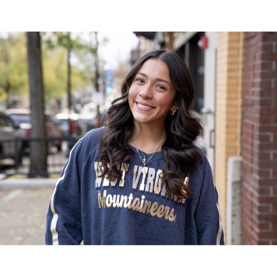 Model wearing the navy WVU women's crew sweatshirt with a WVU Mountaineers gold foil and glitter full front print and gold twill taping down sleeves