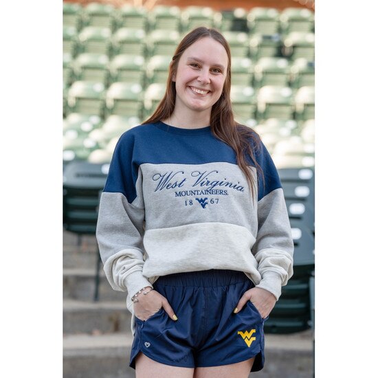 Model wearing the navy WVU women's high waisted shorts with a Flying WV Logo lightweight rubberized print at lower left leg along with a color-blocked grey and navy WVU crew sweatshirt