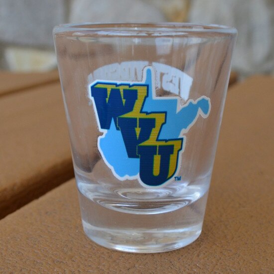 Clear WVU football throwback shot glass sitting on a table