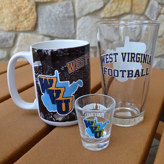 Group photo of the three WVU football throwback glassware; white mug, pint glass, and the shot glass